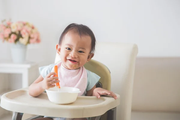 baby girl sitting on high chair and feed her self