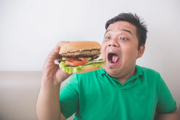 Lelaki gemuk makan hamburger di rumah — Stok Foto