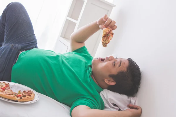 침대에 누워 있는 동안 먹는 게으른 비만 남자 피자 — 스톡 사진