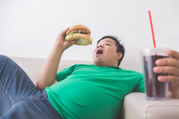 Leniwy otyły człowiek spożywa żywności wiadomości-śmieci podczas r. na kanapie — Zdjęcie stockowe