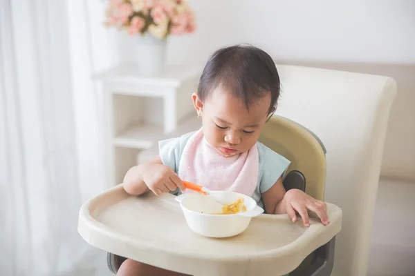 Bambina seduta sul seggiolone e nutrire se stessa — Foto Stock