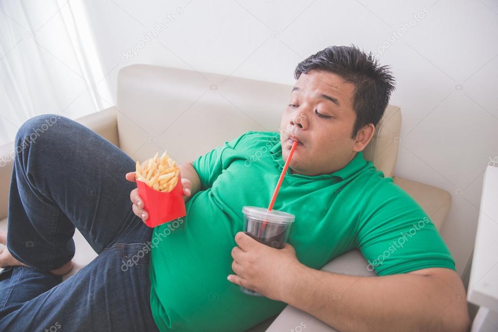 Lazy obese person eats junk food while laying on a couch — Stock ...