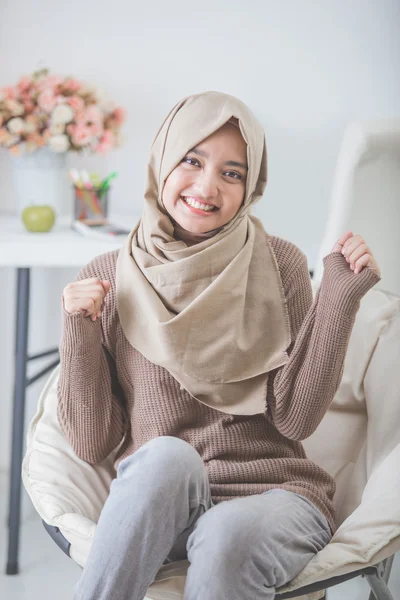 Upphetsad ung kvinna med hijab leende medan du sitter på en soffa — Stockfoto