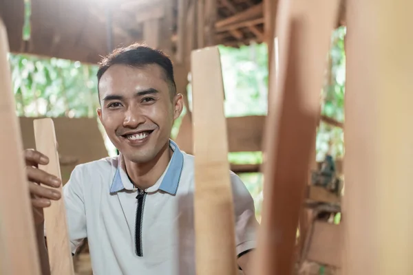 Nahaufnahme eines Tischlers, der lächelnd zwischen den Beinen eines Holzstuhls arbeitet — Stockfoto