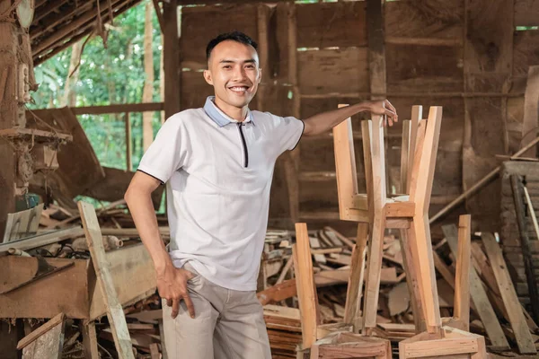 Ο νεαρός επιχειρηματίας χαμογελά με το χέρι στηρίζεται σε ξύλινες καρέκλες, ενώ στέκεται — Φωτογραφία Αρχείου