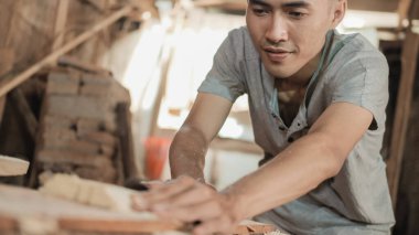 Marangoz dairesel bir testere ile keserken odunu tutuyor.