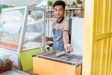 Genç adam ızgara sosis yapıyor.