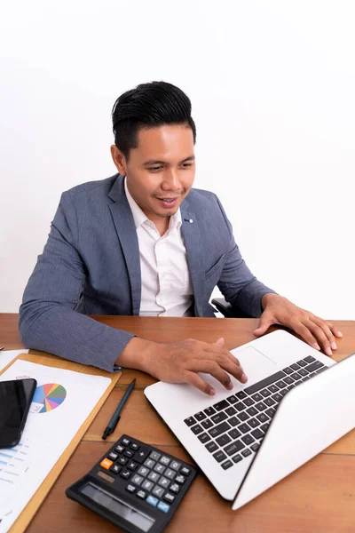 Ένας ελκυστικός και χαρούμενος νέος επιχειρηματίας που εργάζεται σε ένα φορητό υπολογιστή και χαμογελά καθιστός. — Φωτογραφία Αρχείου