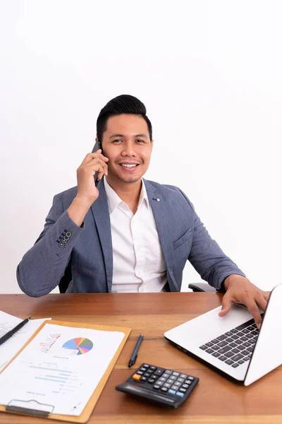 En attraktiv och glad ung affärsman som håller i en mobiltelefon och ler medan han sitter ner. — Stockfoto