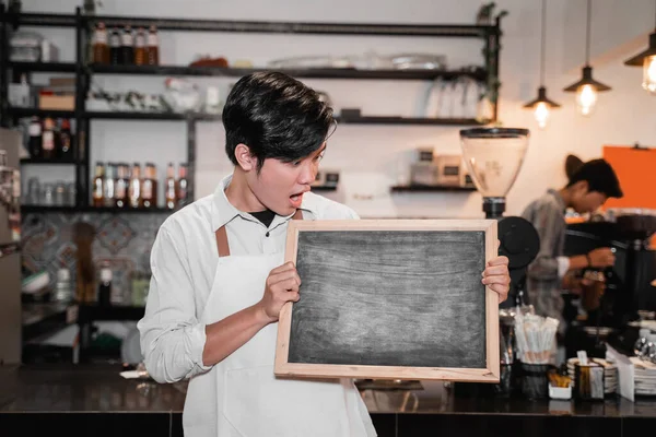 Barista segurando e olhando um quadro negro — Fotografia de Stock