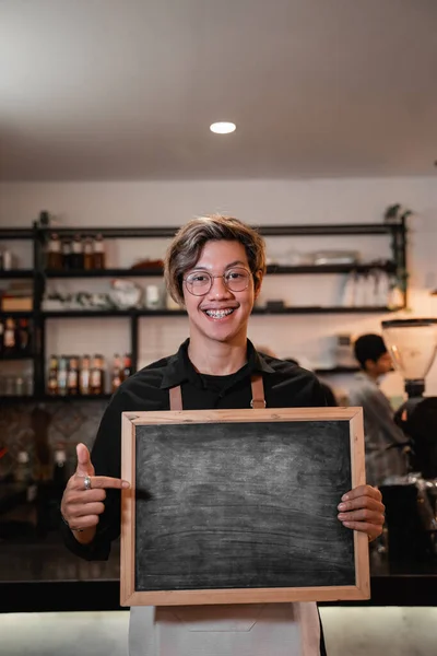 Asiático barista segurando e apontando uma placa — Fotografia de Stock