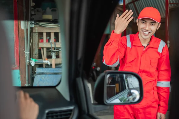 Nahaufnahme des Mechanikers in roter Uniform mit Geste nach vorn, wenn der Kunde ankommt — Stockfoto