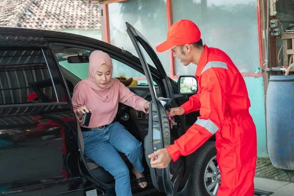 赤い制服を着たアジアの男は、顧客が修理のために車で来るときにドアを開くのに役立ちます — ストック写真