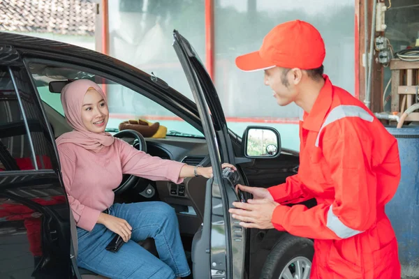 O mecânico de uniforme vermelho abre a porta do carro quando o cliente chega ao carro para ser reparado — Fotografia de Stock