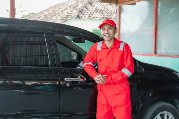 Asiático coche lavadora usando rojo uniforme sonriendo inclinado en el coche después de terminar de lavar el coche —  Fotos de Stock