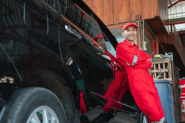 Asian car washer wearing red uniform is standing leaning against the car — Stock Photo, Image