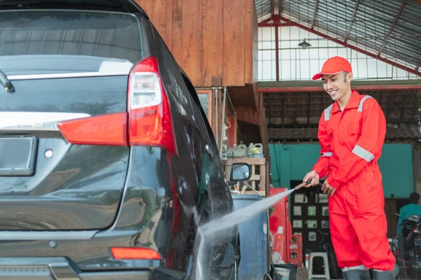 Um limpador de carro usando um uniforme vermelho pulveriza água de alta pressão usando uma mangueira nos pneus — Fotografia de Stock