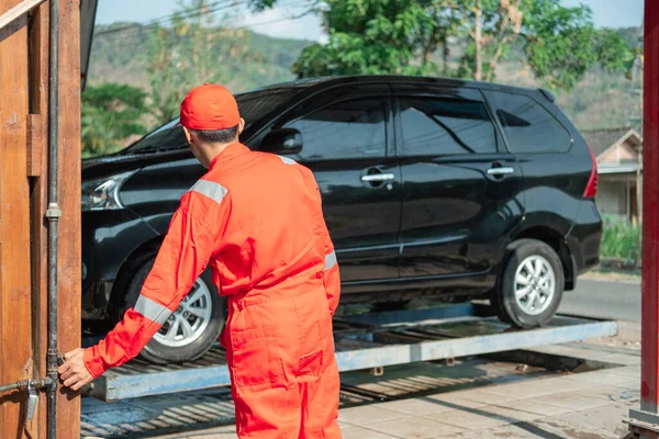 Limpador de carro masculino vestindo o uniforme vermelho eo chapéu definir a torneira para elevar a hidráulica do carro — Fotografia de Stock