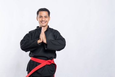 Pencak Silat üniformalı bir adam iki eli göğsünün önünde saygılı bir şekilde poz verir.