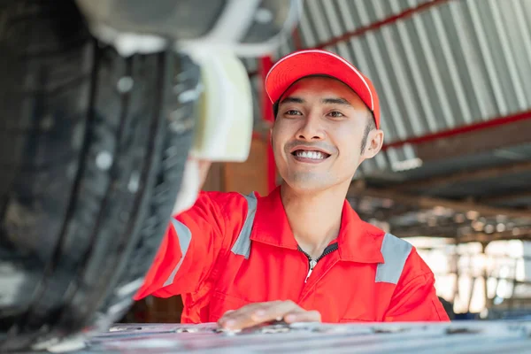 Limpiador de coche masculino usa uniforme rojo y sombrero sonriente mientras lava neumáticos —  Fotos de Stock