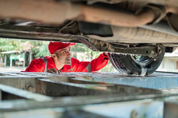 Male car cleaner wearing the red uniform looks under the car while washing the car — Stock Photo, Image