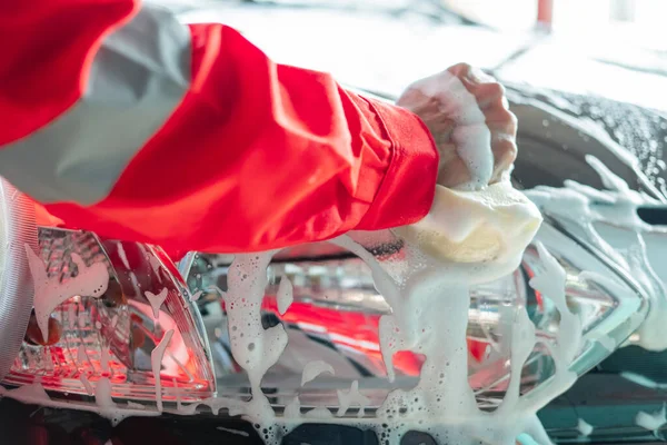 close up of car cleaner hands in red uniforms cleaning car windows with a foamy sponge