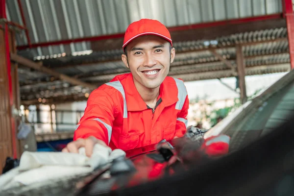 selective focus of car cleaner Asian male wearing red uniform smiling while wiping the car