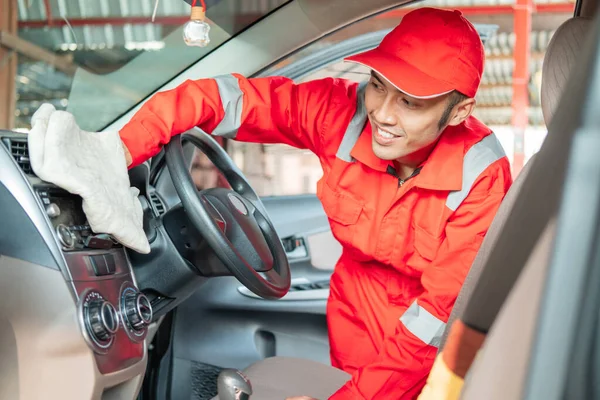 Mężczyzna samochód sprzątaczka noszenie czerwony mundur to wycieranie samochód wnętrze deska rozdzielcza — Zdjęcie stockowe