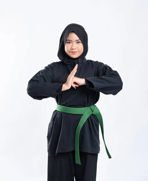 Een vrouw met capuchon draagt een pencak silat uniform met een groene riem en voert respectvolle handgebaren uit — Stockfoto