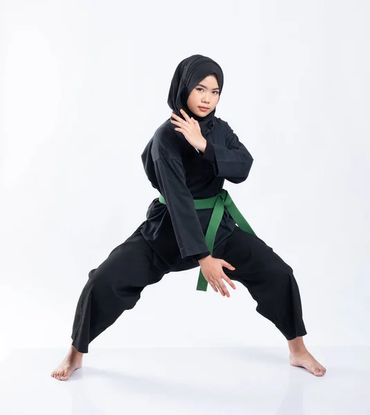 A veiled woman wears a pencak silat uniform with a green belt with a middle stance — Stock Photo, Image