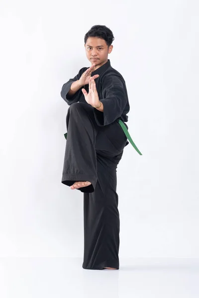 Ung asiatisk man i pencak silat uniform med en fot upp med båda händerna redo — Stockfoto