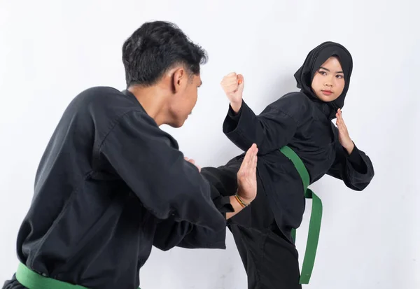 Visão traseira de um homem vestindo um uniforme de seda pencak de pé com um movimento para bloquear os chutes de uma mulher asiática em um véu — Fotografia de Stock
