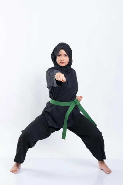 En kvinna i slöja i en pencak silat uniform utgör en medelställning och blåser framåt — Stockfoto