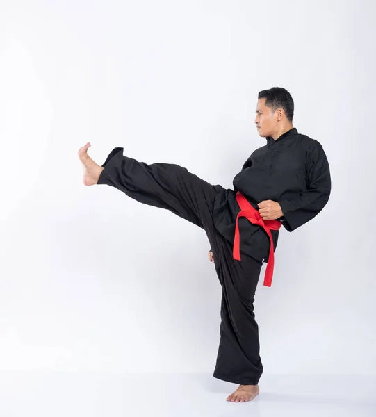 Vista lado de um homem asiático com um ataque pose chutando para a frente enquanto vestindo um pencak silat uniforme — Fotografia de Stock