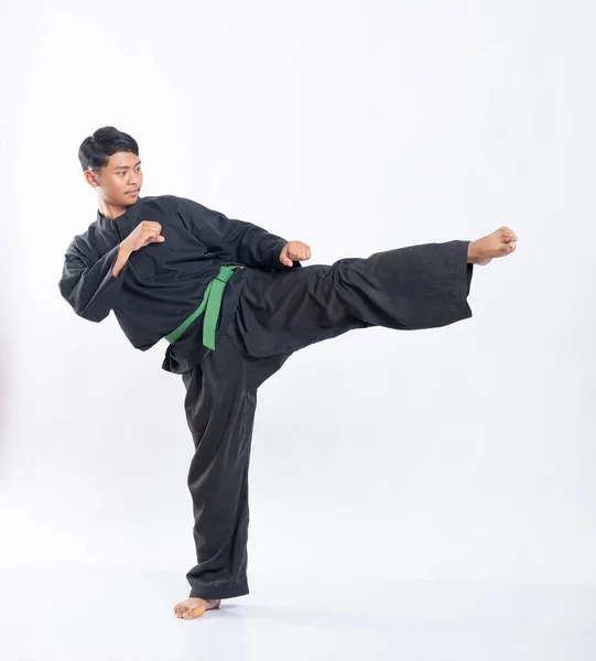 Asiáticos vestidos con uniformes de pencak silat con cinturones verdes pateando una pierna a un lado — Foto de Stock