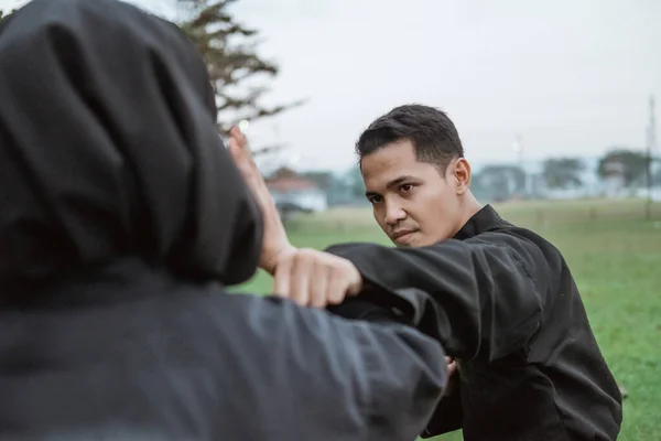 Young Asian men wearing pencak silat uniforms with punching movements and women wearing hijabs with a tangkisan movement — Stock Photo, Image