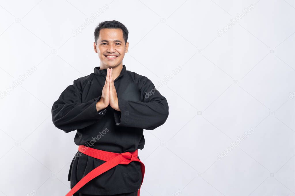 man in pencak silat uniform poses respectfully with both hands cupped in front of his chest