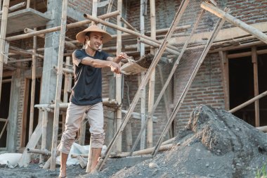 Mason, ellemek için kum taşırken küreği tutuyor.