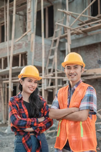 male and female contractors standing with crossed hands smiling at the camera wearing safety helmets
