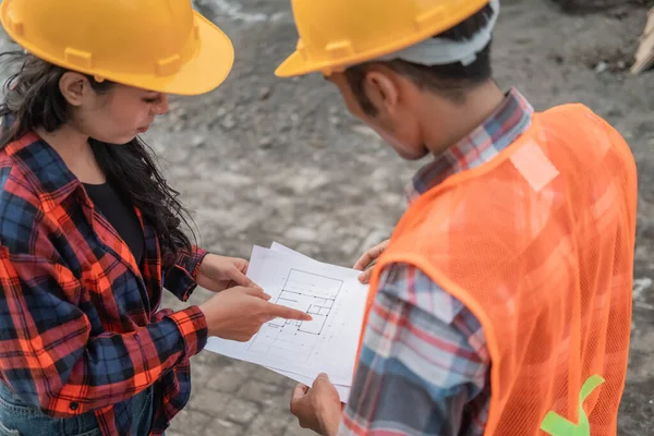 male and female asian contractors wearing safety helmets holding the site plan building