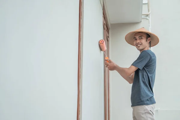 Un peintre avec un chapeau peint à l'aide d'un rouleau de peinture — Photo
