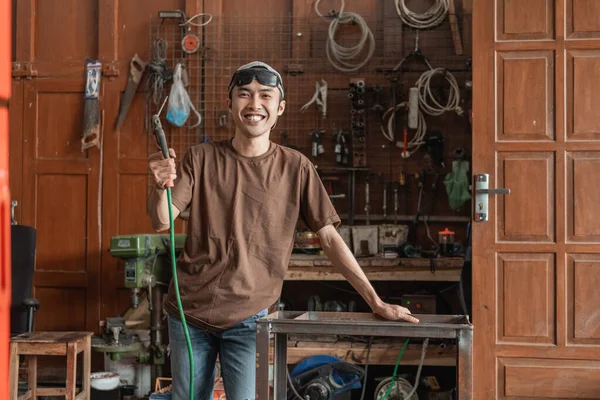 Sonriente soldador mira a la cámara mientras sostiene un soldador eléctrico —  Fotos de Stock