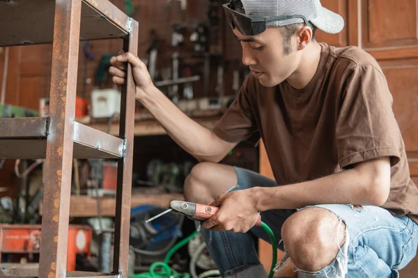 Азиатский сварщик держит железную стойку при сварке с помощью электросварщика — стоковое фото