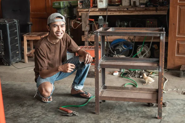 Soldador macho sonriente en cuclillas después de usar soldadura eléctrica para soldar el marco metálico —  Fotos de Stock