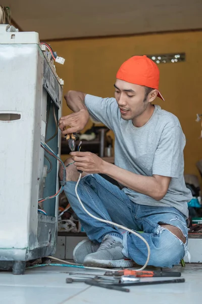 Ázsiai elektronikai dolgozók fogóval rögzítse a mosógép kábel, hogy eltört, miközben guggolt — Stock Fotó