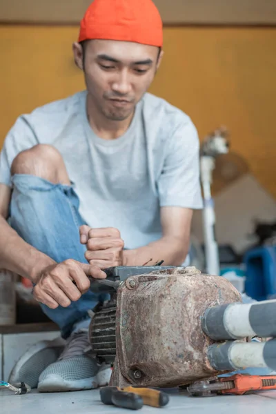 Asyalı erkek elektronik işçisi su pompası makinesini tamir ederken vidayı sökmek için üç anahtar kullanır — Stok fotoğraf