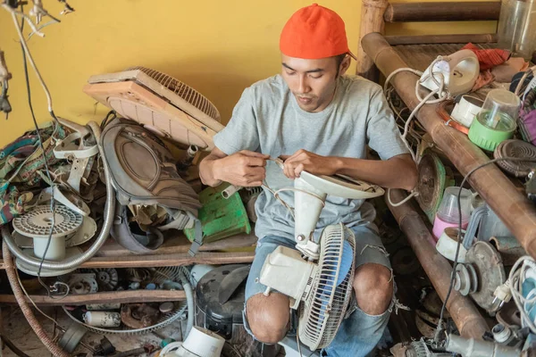 Electronics repairmen repair fan wiring while sitting around broken items