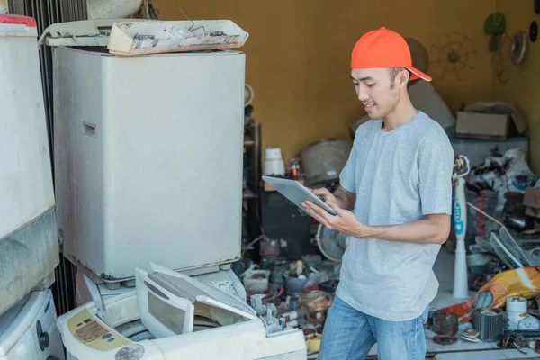 Reparador de electrónica asiática utiliza una tableta PC, mientras que de pie alrededor de la electrónica rota —  Fotos de Stock