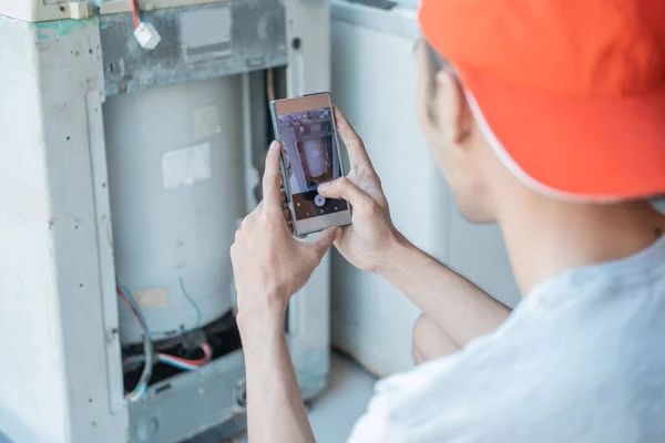 Ázsiai elektronikus szerelő készít egy képet a mosógép sérüléséről egy mobiltelefon kamera segítségével — Stock Fotó