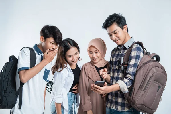 Retrato de jóvenes universitarios felices llevando bolsos y discutiendo mirando teléfonos celulares —  Fotos de Stock